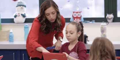 A teacher leaning over to help a student who is working on an iPad.