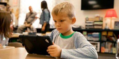 A young boy sitting at a desk looking at a tablet.
