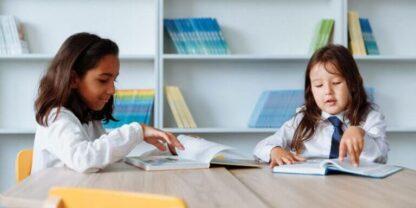 Two young girls sitting at a table working on reading activities together.